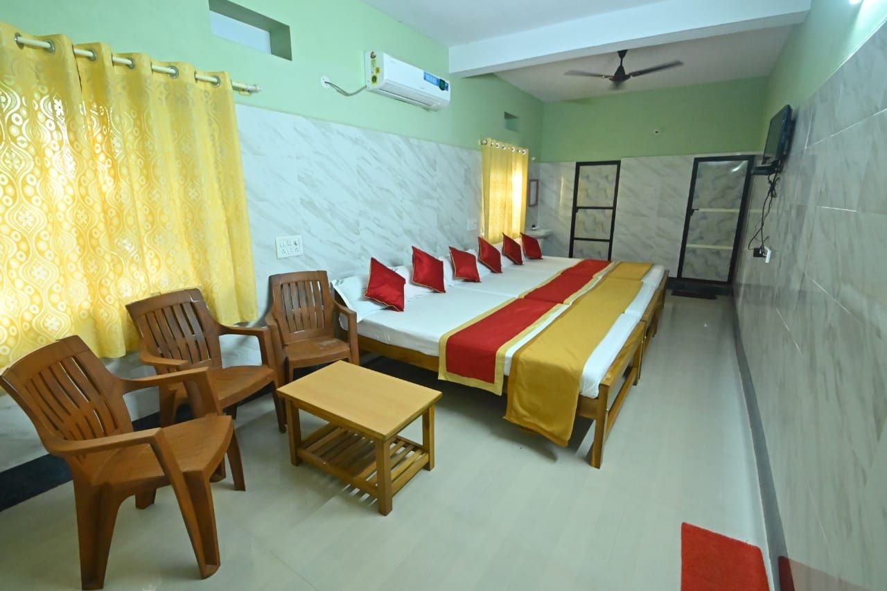 Habitación de hotel con cama, sillas, una mesa, aire acondicionado, ventilador de techo y televisor.