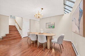 A dining area with a round table, four chairs, a chandelier, and a staircase leading to another room. - 4BR Family Home | Rooftop Views | UBC & Downtown (Vancouver)