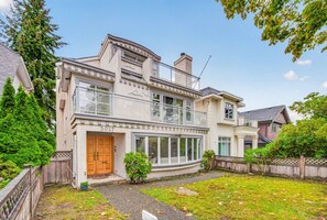 A two-story house with a garage, a front porch, and a well-maintained lawn. - 4BR Family Home | Rooftop Views | UBC & Downtown (Vancouver)