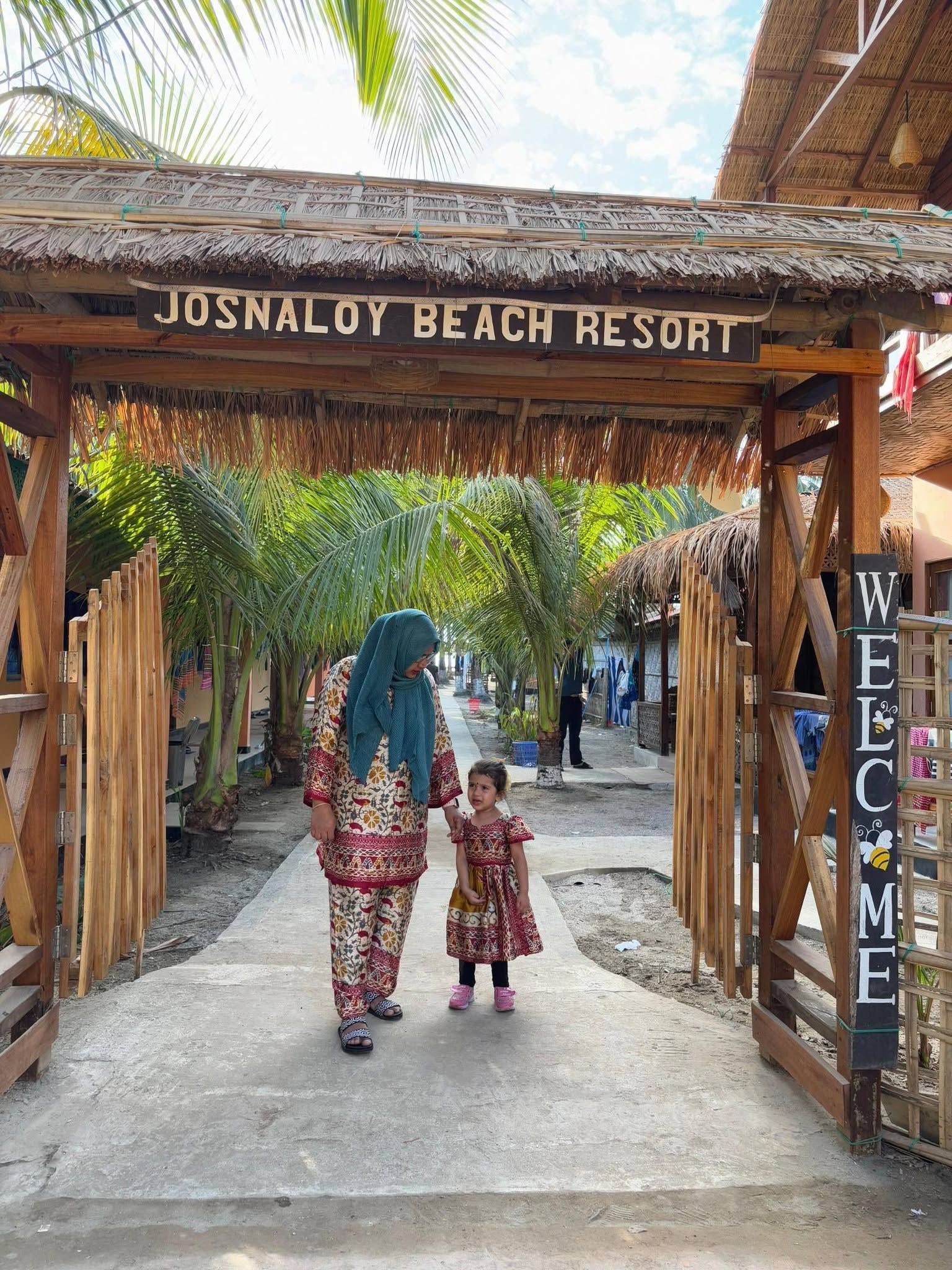 Um arco de madeira com a placa 'JOSNALOY BEACH RESORT' e um letreiro de 'BEM-VINDO'.