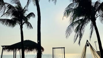 Uma praia com palmeiras, um deck de madeira e uma estrutura com telhado de palha.