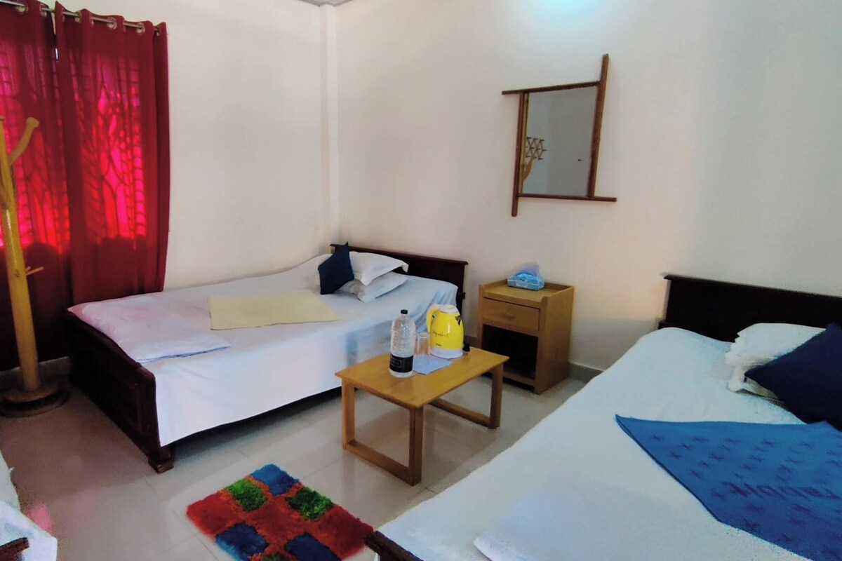 Quarto de hotel com duas camas, uma mesa de madeira pequena, um criado-mudo, um espelho e uma cortina vermelha.