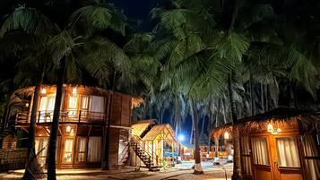 A beachfront resort with thatched-roof cabins, palm trees, and a sandy walkway.