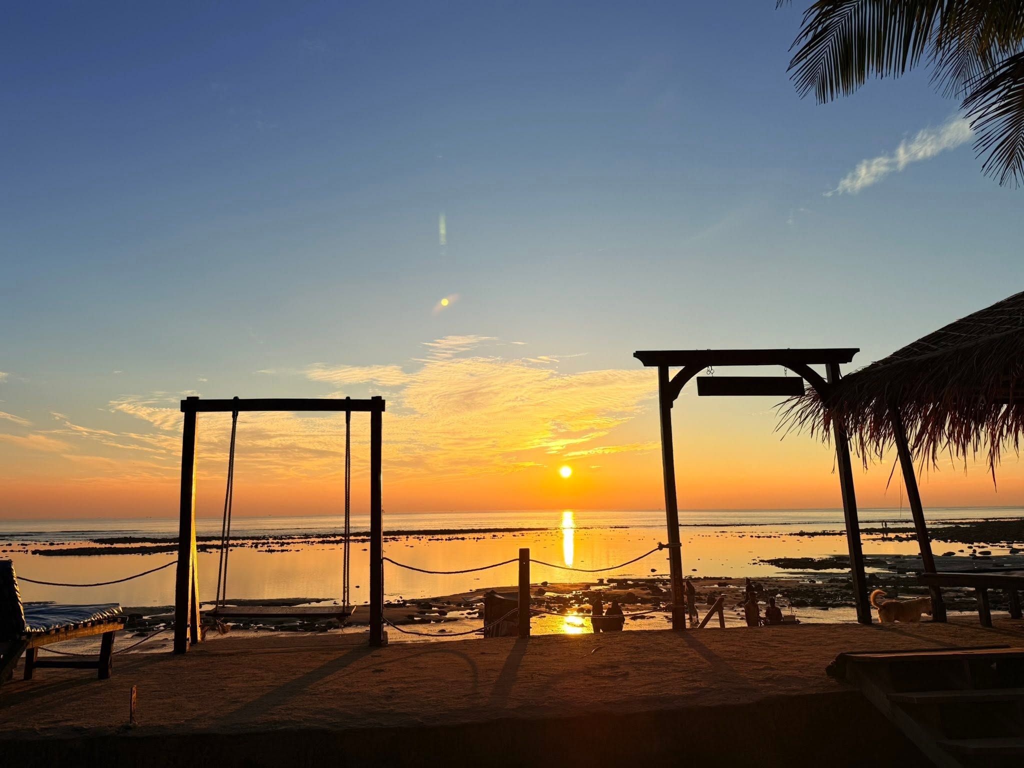 A beach scene with a swing set and a shaded area at sunset.
