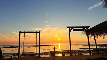 A beach scene with a swing set and a shaded area at sunset.