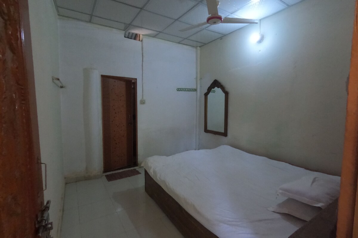 Quarto com cama, ventilador de teto, porta e espelho fixado na parede.
