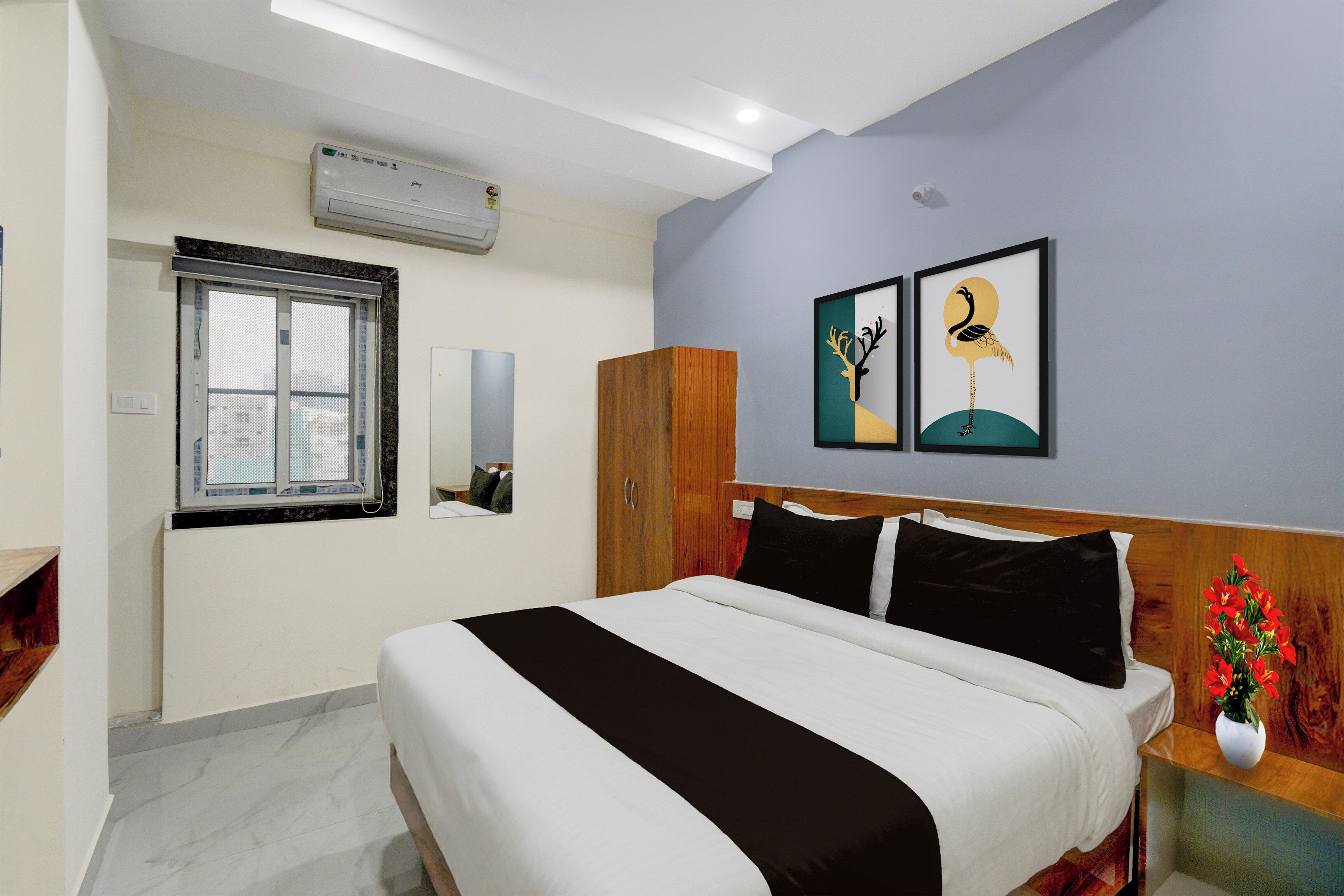 Een hotelkamer met een bed, een raam, een airconditioning en een kledingkast, plus twee kunstwerken in lijsten aan de muur.