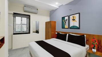 Een hotelkamer met een bed, een raam, een airconditioning en een kledingkast, plus twee kunstwerken in lijsten aan de muur.