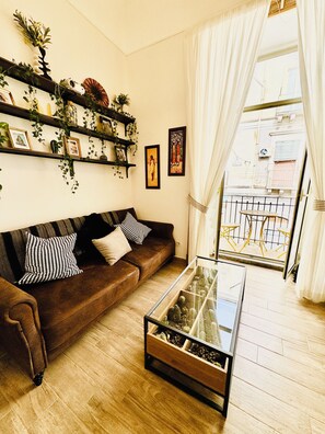A living room with a brown sofa, a glass coffee table, and a balcony with a metal railing. - New Listing (Catania)