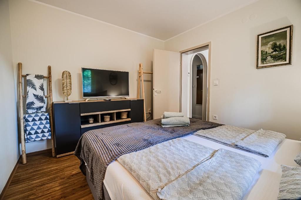 A bedroom with a bed, a TV on a stand, a wardrobe, and a door leading to another room.