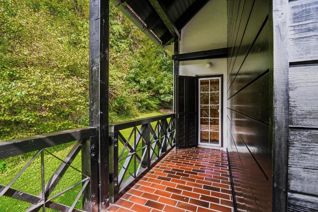 A covered wooden deck with a brick floor, surrounded by greenery.