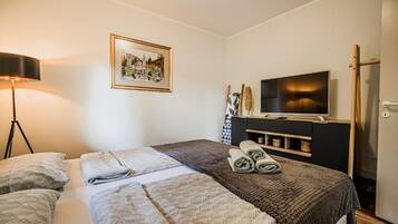 A hotel room with two beds, a television, a framed picture on the wall, and a lamp.