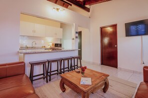 Una sala de estar moderna con una mesa de centro de madera, sofá de cuero y una zona de cocina con armarios blancos y un microondas.