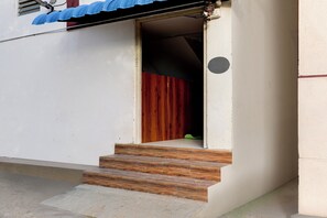 A set of wooden steps leading to a doorway with a red interior, a white exterior wall, and a blue roof.