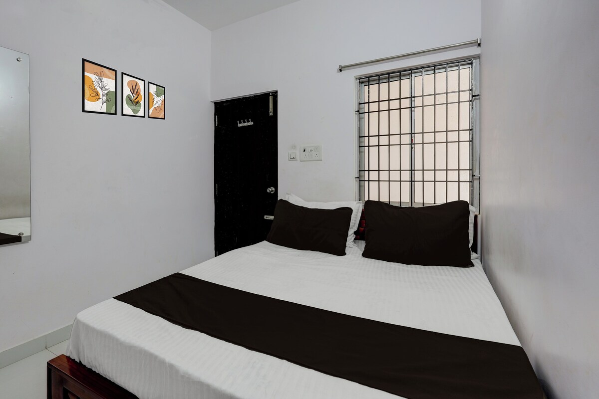 A bedroom with a bed, a door, a window with bars, and three framed pictures on the wall.