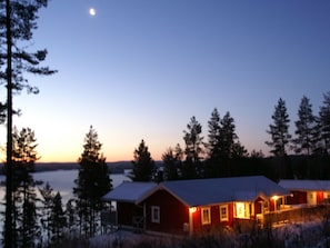 A cabin with a snow-covered roof, surrounded by trees and a body of water. - Holiday Home in Algana With Swimming Pool (Årjäng)