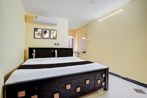 A hotel room with a bed, air conditioning unit, framed artwork, and a mirror.