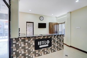 Una recepción de hotel con un reloj, un televisor de pantalla plana y un letrero que indica que el servicio es proporcionado por la empresa.
