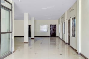 Un largo pasillo con paredes blancas, piso de baldosas y varias puertas y ventanas.