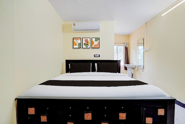 Una habitación de hotel con cama, aire acondicionado instalado en la pared, ventana con cortinas y lavamanos también en la pared.