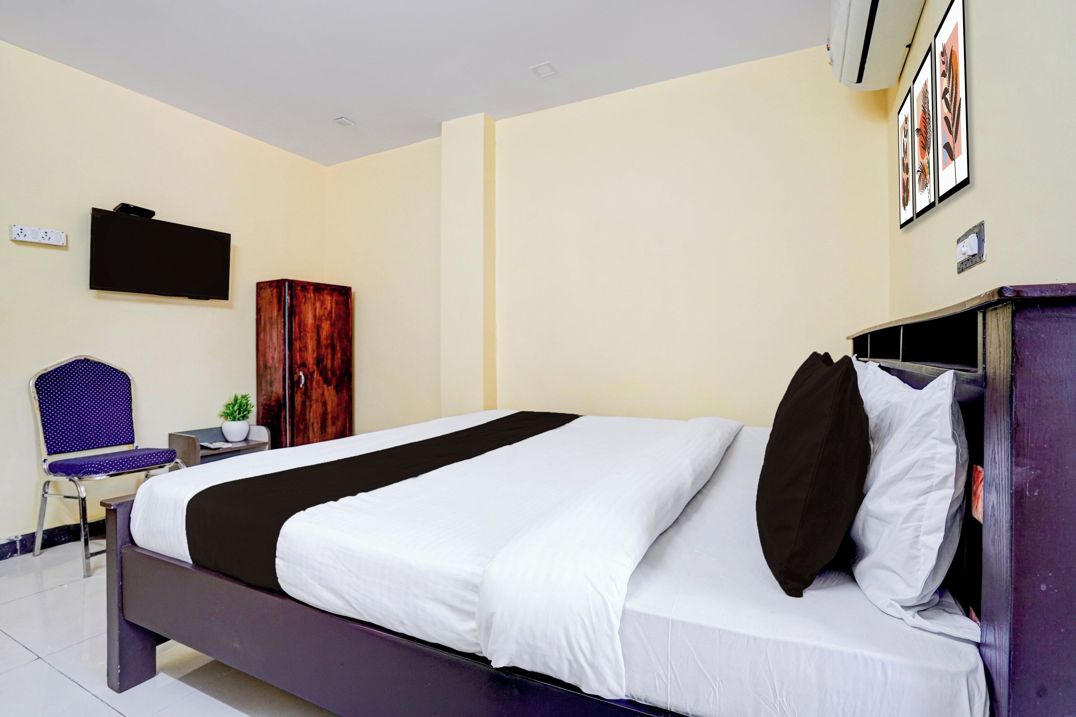 A hotel room with a bed, a chair, a wardrobe, a TV, and a wall-mounted air conditioner.