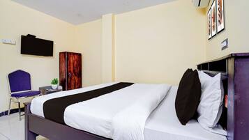 A hotel room with a bed, a chair, a wardrobe, a TV, and a wall-mounted air conditioner.