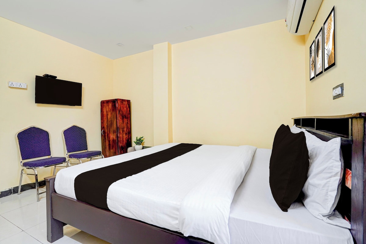 A hotel room with a bed, a television, a wardrobe, and two chairs.