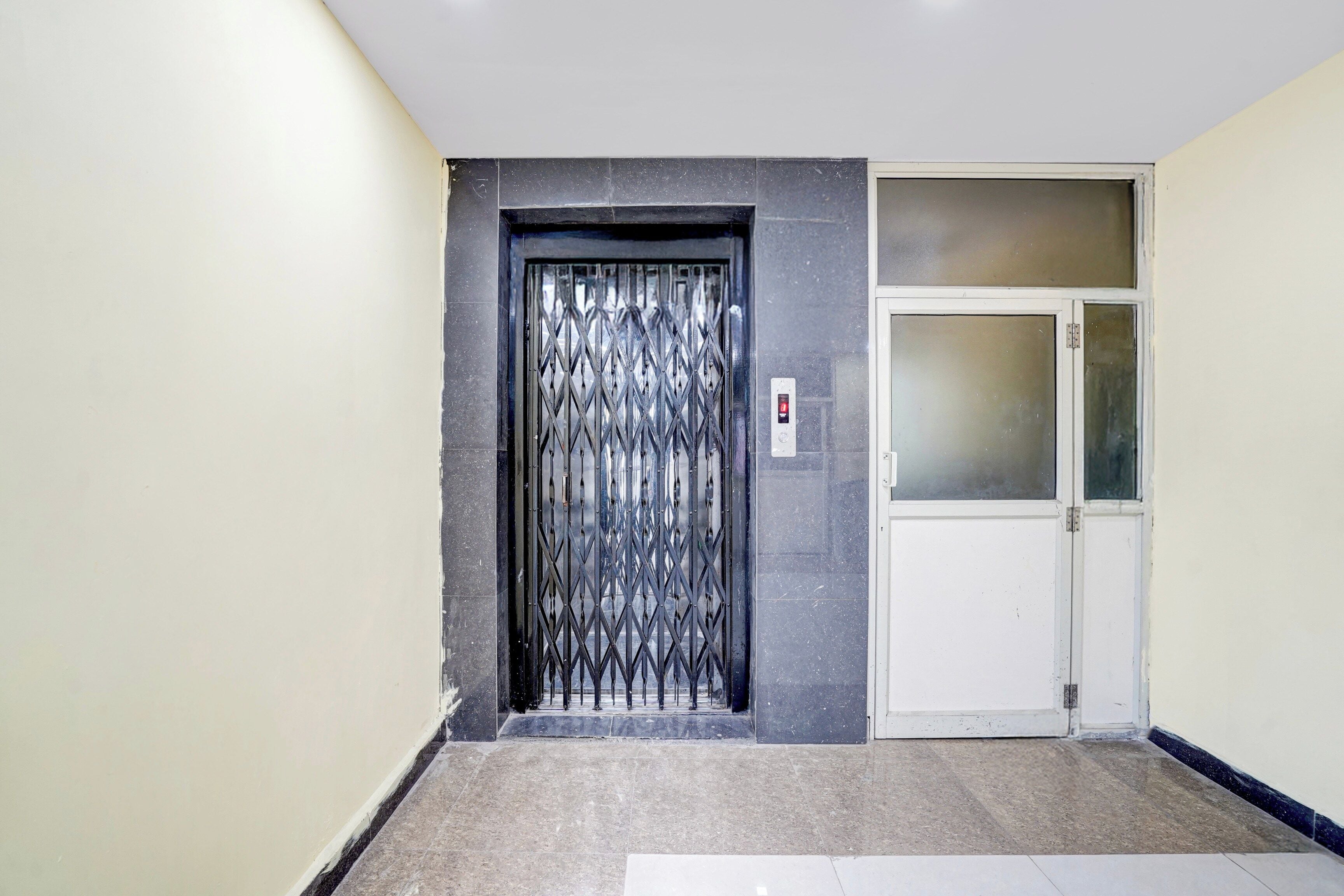 Un couloir avec une porte-grille en métal et une porte blanche dotée de panneaux en verre dépoli.