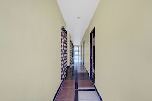 A long, narrow hallway with patterned curtains on one side and doors on the other, leading to an open area at the end.
