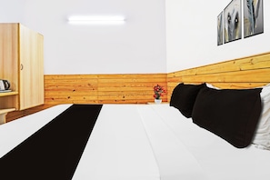 Una habitación de hotel con una cama, un armario de madera, una mesita de noche con un florero y un cuadro colgado en la pared.