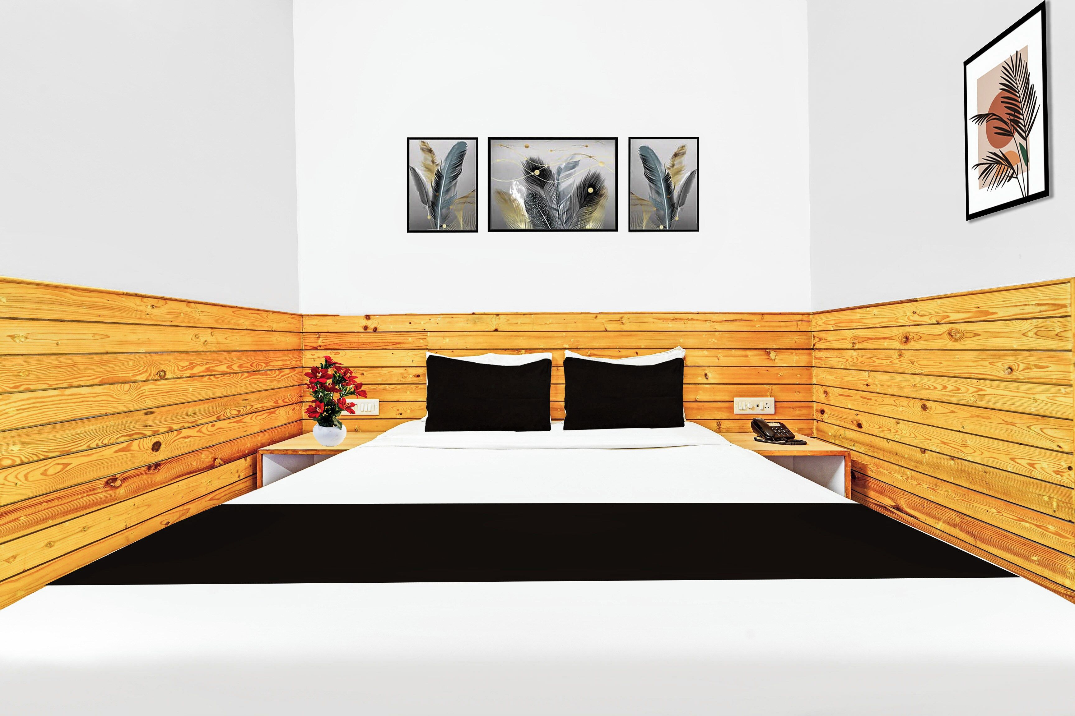 Quarto de hotel com painel de parede em madeira, cama com roupa de cama preta, mesa de cabeceira com telefone e três obras de arte emolduradas acima da cama.