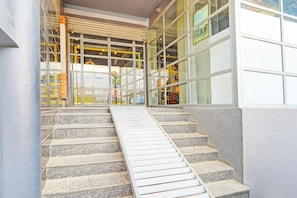 Un conjunto de escalones de piedra que conducen a la entrada de un edificio con ventanas grandes y una rampa de metal.