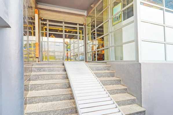 A set of stone steps leading to a building entrance with large windows and a metal ramp.