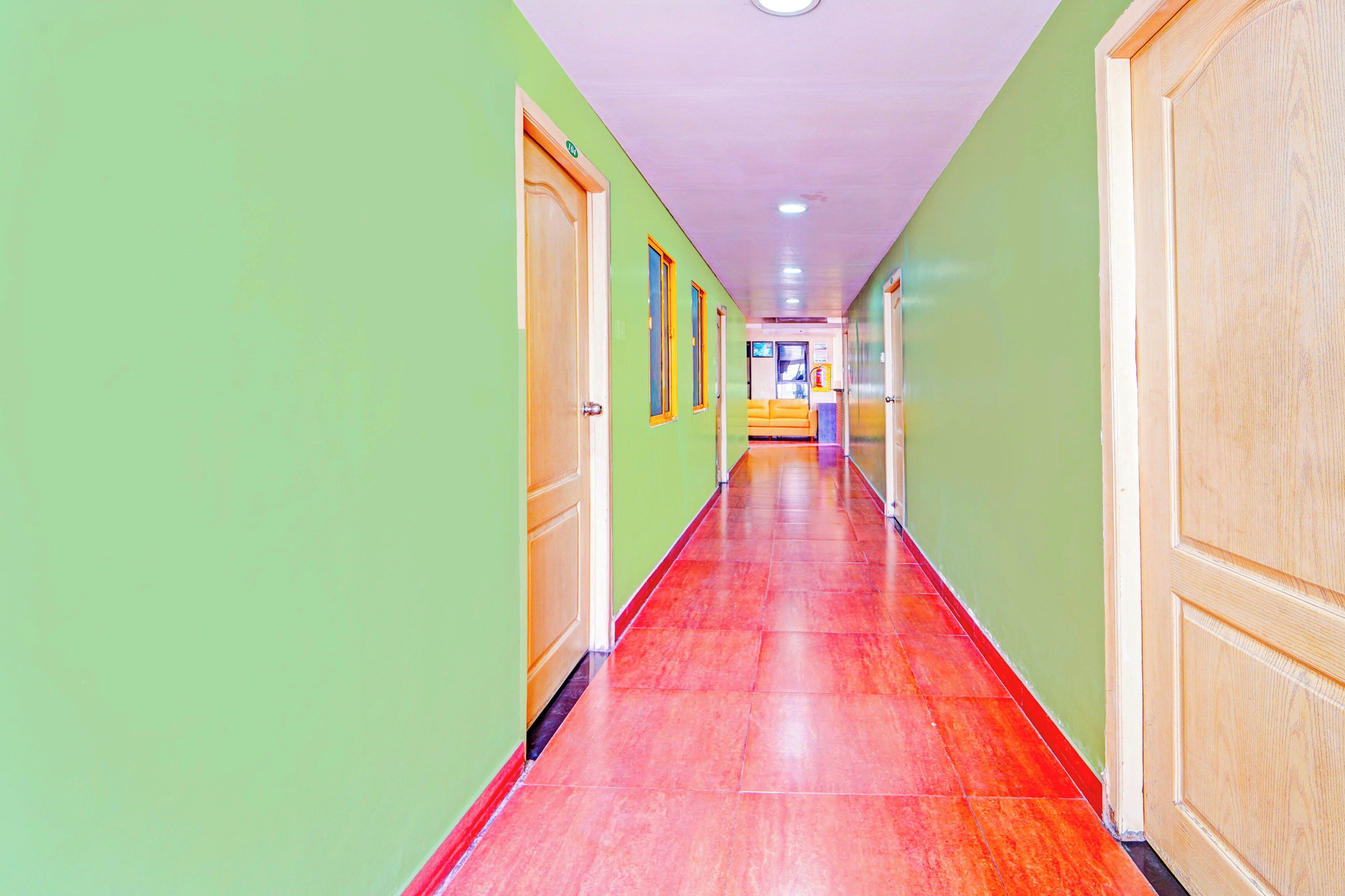 A long, narrow hallway with green walls and red flooring, leading to a room with a yellow sofa.