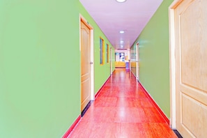Un pasillo largo y estrecho con paredes verdes y piso rojo, que conduce a una habitación con un sofá amarillo.