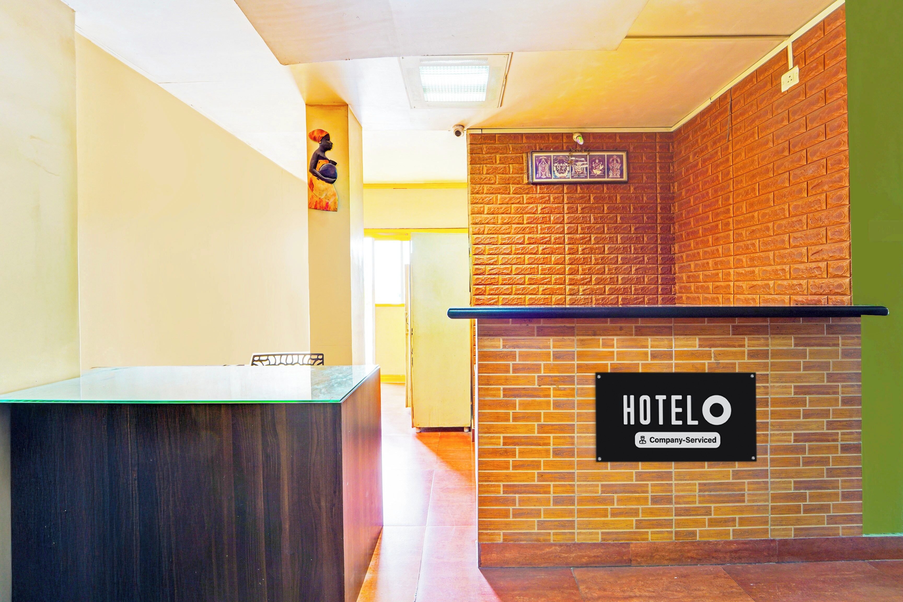 Un hall d'hôtel comprenant un comptoir d'accueil, une enseigne indiquant « HÔTEL » et un mur en briques orné d'un tableau encadré.