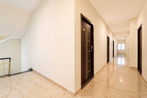 A hotel corridor with a marble floor, dark wooden doors, and a staircase on the left. - Townhouse Erode Bus Terminal (Erode)