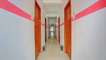 A long, narrow hallway with doors on both sides, leading to rooms. The hallway has a tiled floor and is lined with potted plants.