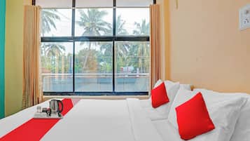 A hotel room with a large bed, red pillows, a coffee maker, and a view of palm trees through a window.