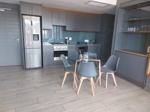 A modern kitchen with a built-in oven, a refrigerator, and a dining area with a table and chairs. - Luxurious 2-Bedroom Apartment in uMhlanga, South Africa (uMhlanga)