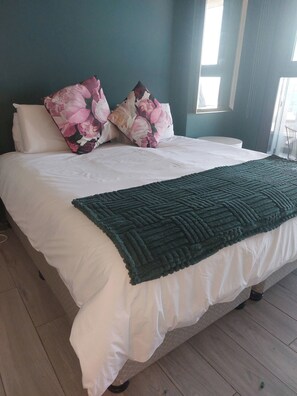 A bed with white bedding, a dark green throw, and floral pillows. - Luxurious 2-Bedroom Apartment in uMhlanga, South Africa (uMhlanga)