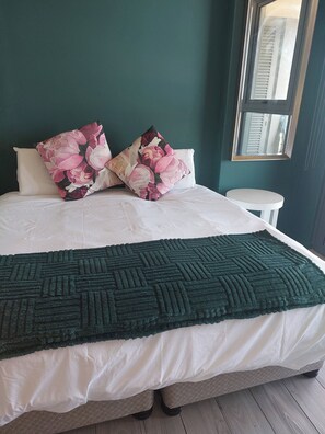 Ein Bett mit weißer Decke, zwei Kissen mit Blumenmuster und einer grünen, gemusterten Tagesdecke.