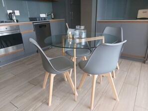 A modern kitchen with a glass dining table, grey chairs, and stainless steel appliances. - Luxurious 2-Bedroom Apartment in uMhlanga, South Africa (uMhlanga)