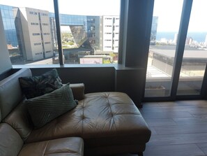 A leather sofa with a cushion and a view of a cityscape through large windows. - Luxurious 2-Bedroom Apartment in uMhlanga, South Africa (uMhlanga)