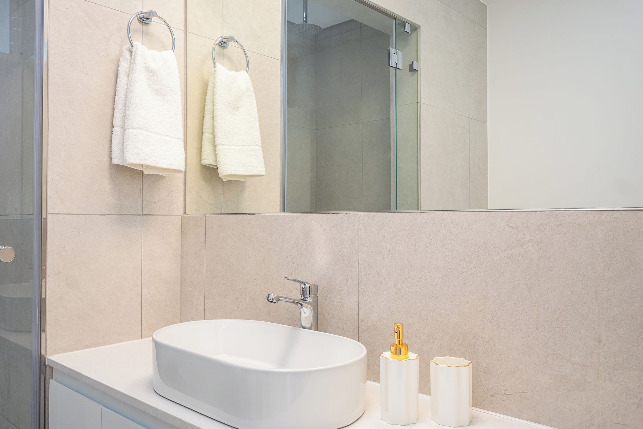 A modern bathroom with a large white sink, a mirror, and two white towels hanging on towel rings.