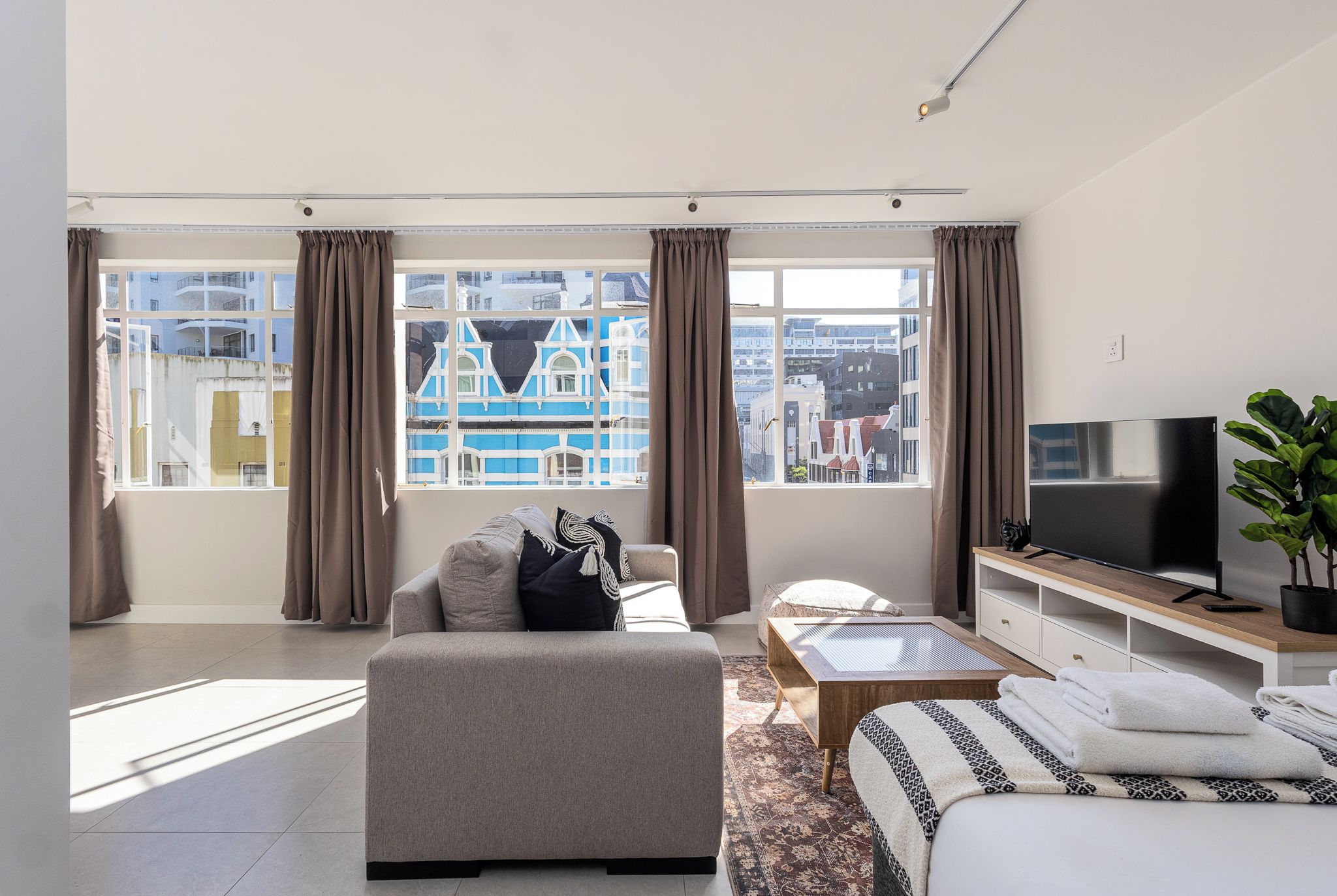 A modern hotel room with a large window, a sofa, a TV, and a small table.