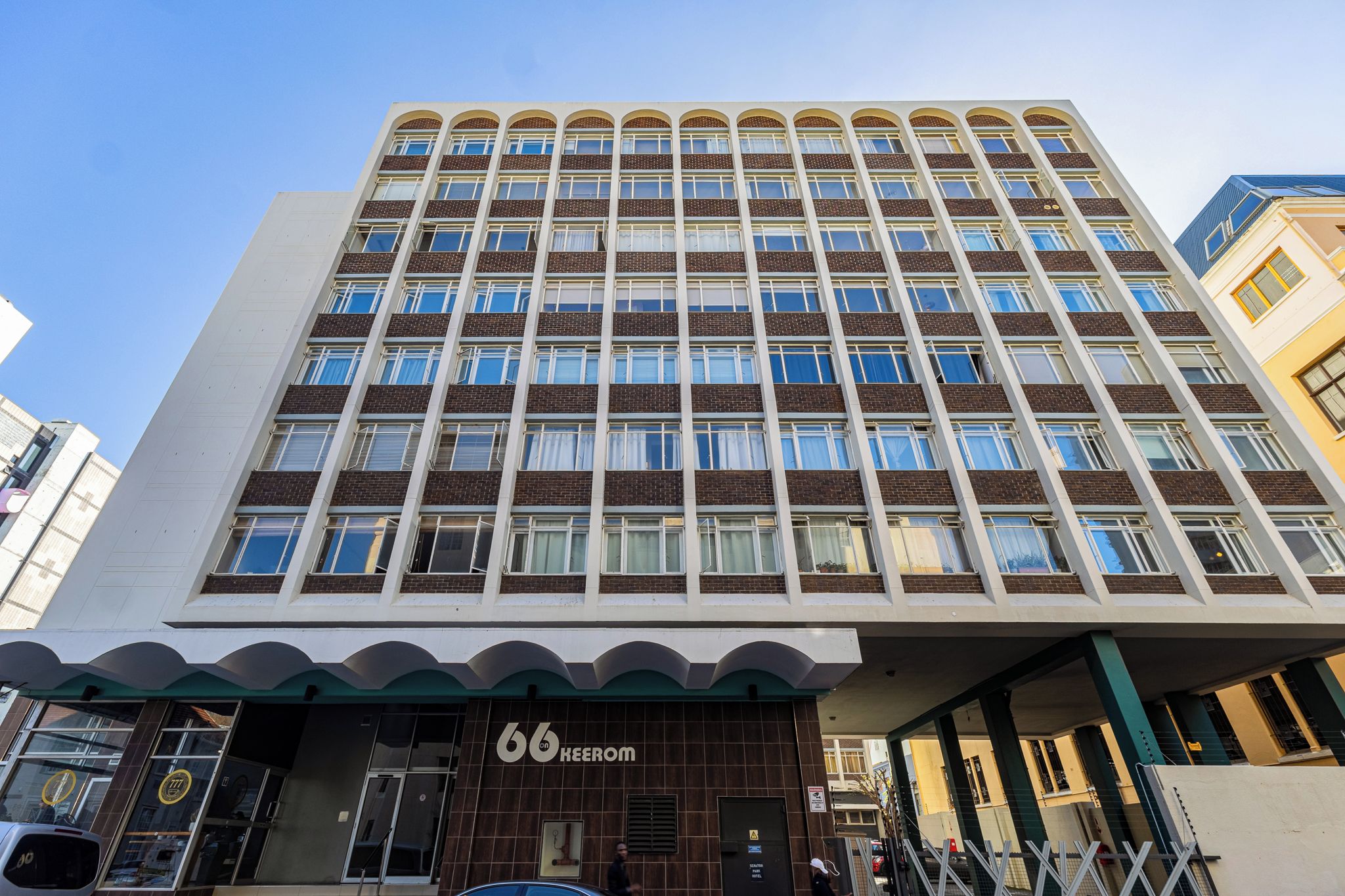 Et hotel med flere etager og en moderne facade, med en markant indgangsparti med en grøn markise og nummeret '66', der angiver hotellets navn.