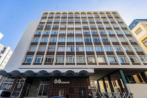 Et hotel med flere etager og en moderne facade, med en markant indgangsparti med en grøn markise og nummeret '66', der angiver hotellets navn.