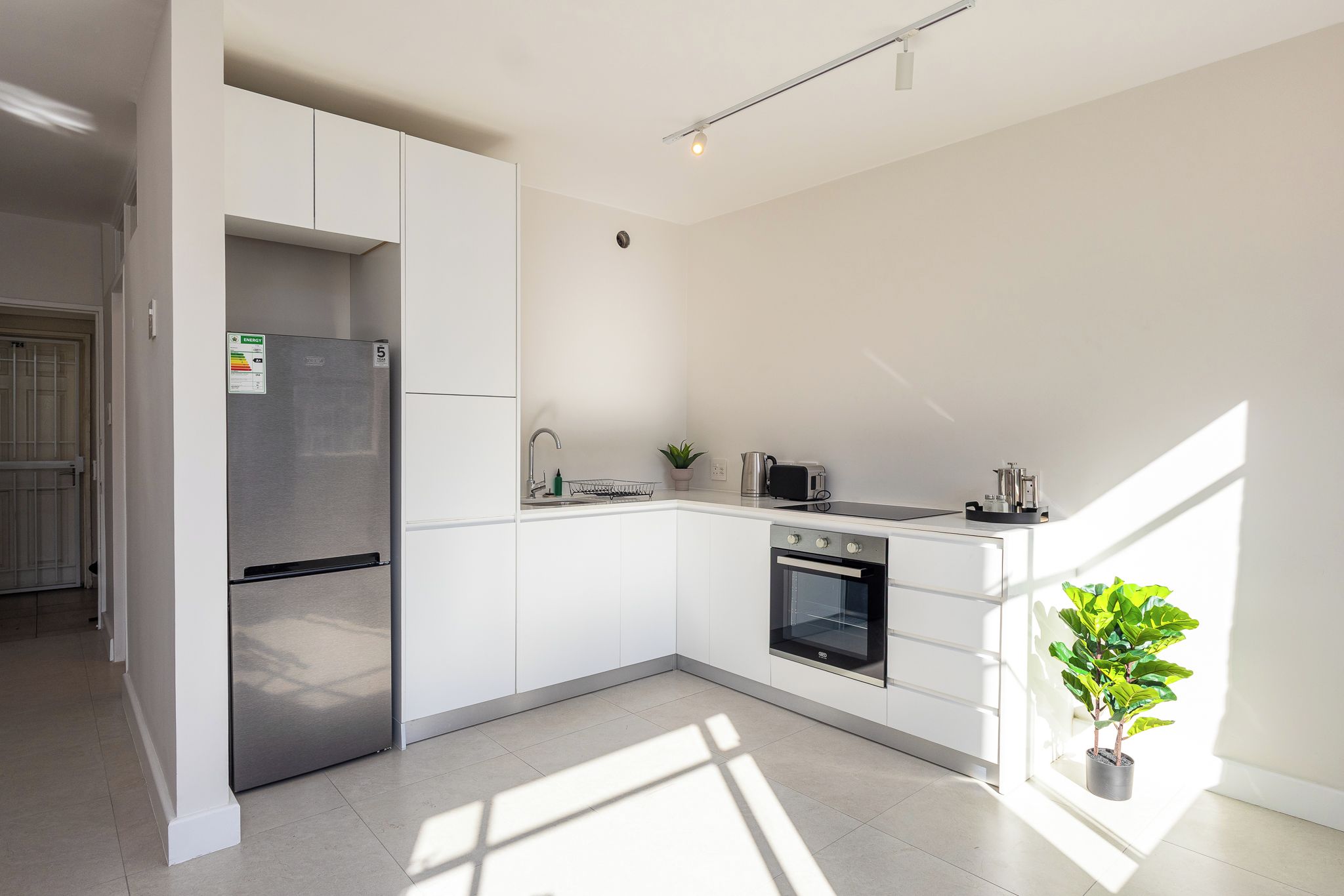 A modern kitchen with white cabinetry, a stainless steel refrigerator, a built-in oven, and a small potted plant.