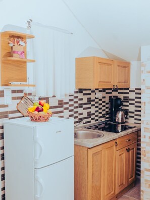 A compact kitchen with a white refrigerator, wooden cabinets, a tiled backsplash, and a basket of fruit on the counter. - Hvar spa & Apartments-1 Bedroom-balcony/sea View 5 (Jelsa)